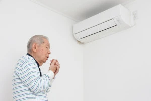 エアコンの前で寒がる老人の写真