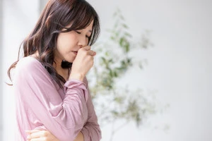 部屋の中で咳をする体調不良の女性の写真