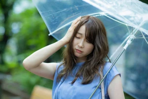 雨の中傘を差して憂鬱そうな女性の写真