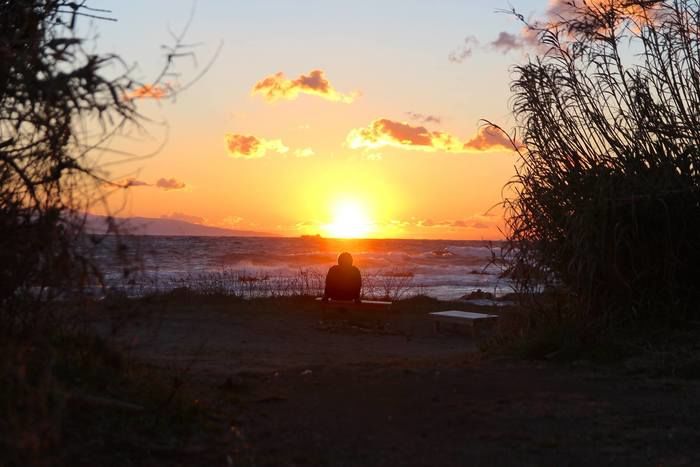 海越しに夕日を見ている人