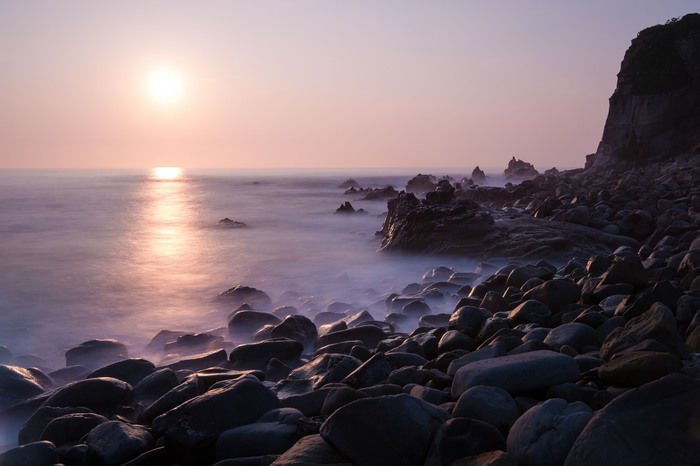 夕日に照らされた海と岩場の写真