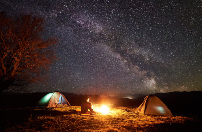 満点の星空の下でテントを貼って焚き火をしている様子の写真
