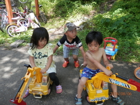 おもちゃの車に乗っている女の子と男の子とその後ろに捕まる男の子