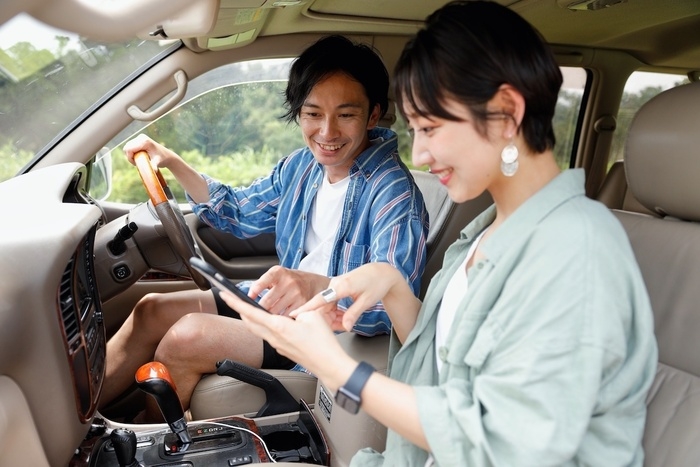 車に乗り、カップルでスマホを見ながら行き先を確認しているところ