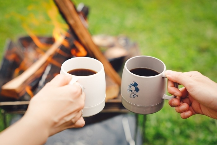 焚き火を前にコーヒーのカップを持っているところ