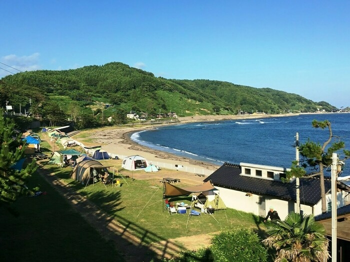 手前に白い平屋の建物とテントサイト、奥には海と山