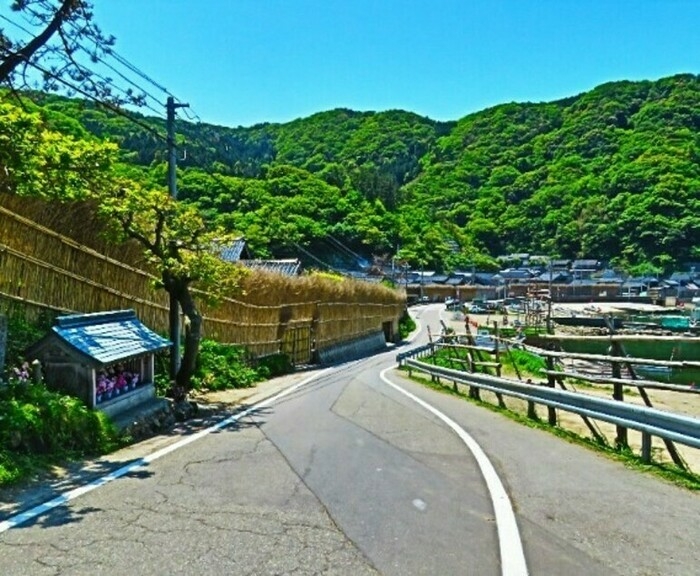 細い生活道路の左に間垣、突き当り遠くに緑豊かな山