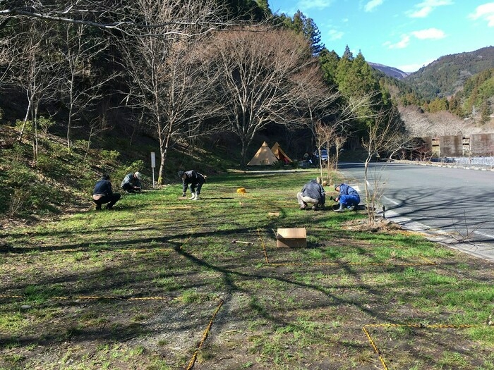 草地をロープで区画分けしている数人の大人