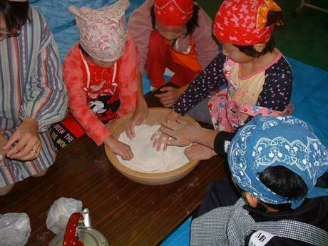 そば粉を混ぜている子ども2人と手伝っている大人3人
