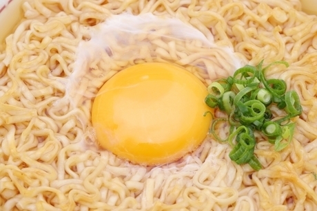 インスタント麺の上にのせた生卵とネギ