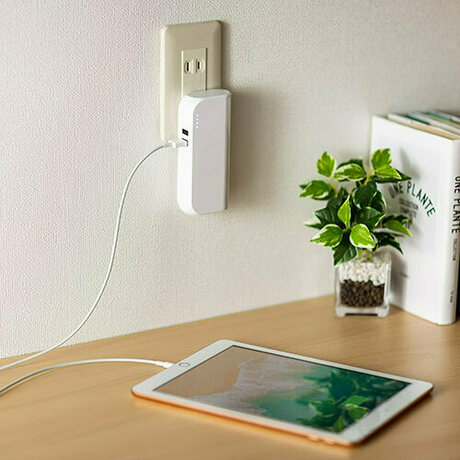 壁のコンセントに差した白いモバイルバッテリーにつないだスマホ