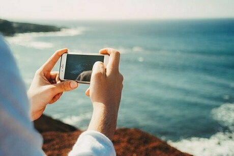 両手でスマホを構えて海を撮影している