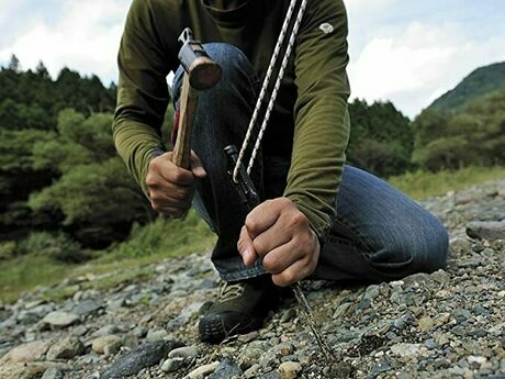 砂利の地面にペグハンマーでペグを打ち込んでいる人