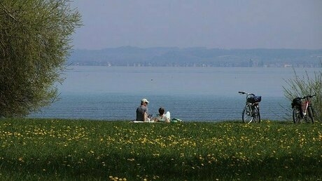 水辺の草原で座って談笑する2人の傍らに自転車2台