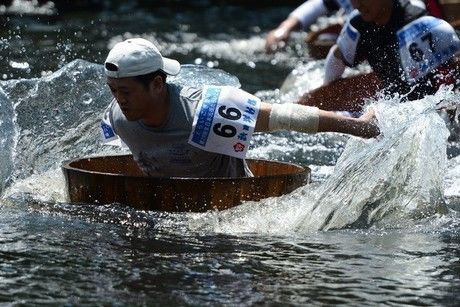 水しぶきを立ててたらいこぎ競争を行う人