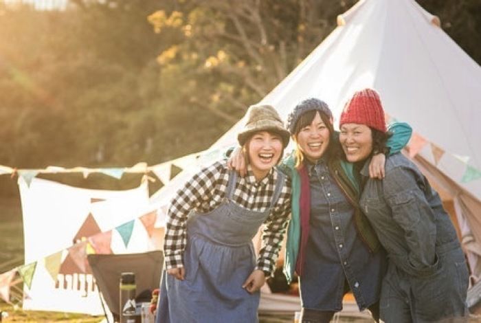 肩を組み笑顔の女性3人とテント