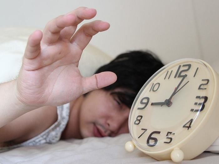 寝起きでめざまし時計をつかもうとする男性