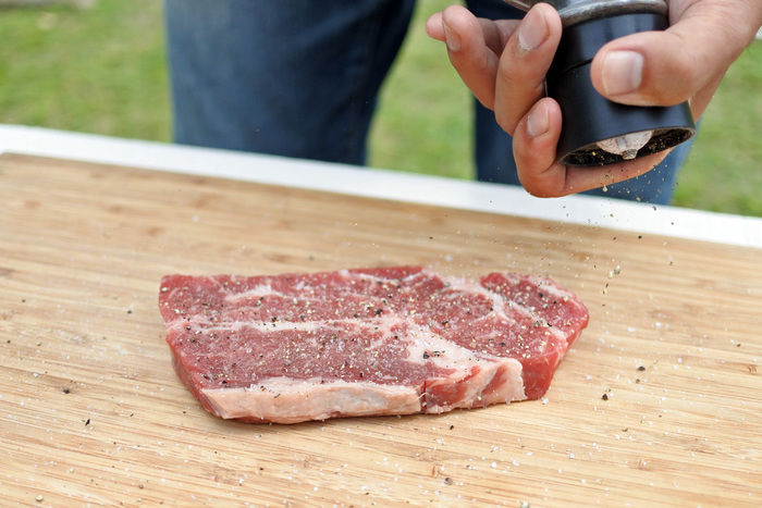 肉にミルで挽いたこしょうをかける様子