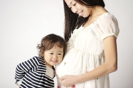 体温が高い妊婦とそのおなかに耳を近づける小さな子供