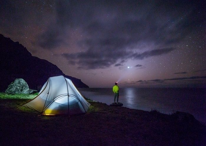湖のすぐそばでソロキャンプをする男性と満天の星