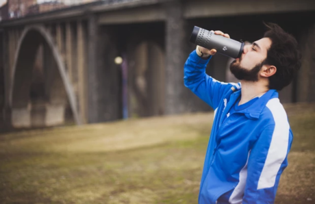 外でたんぶらーで飲み物を飲む男性