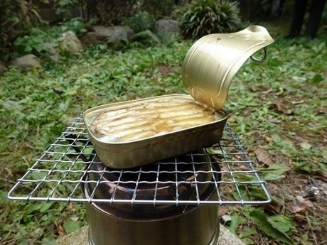 ポータブル薪ストーブの上に網を乗せて缶詰をあたためる様子