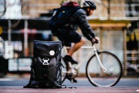 BACKPAIXを背負って自転車に乗る男性と道に置かれたBACKPAIX