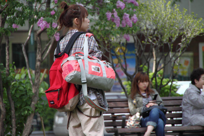 ノースフェイスのバッグを持って街を歩く女性