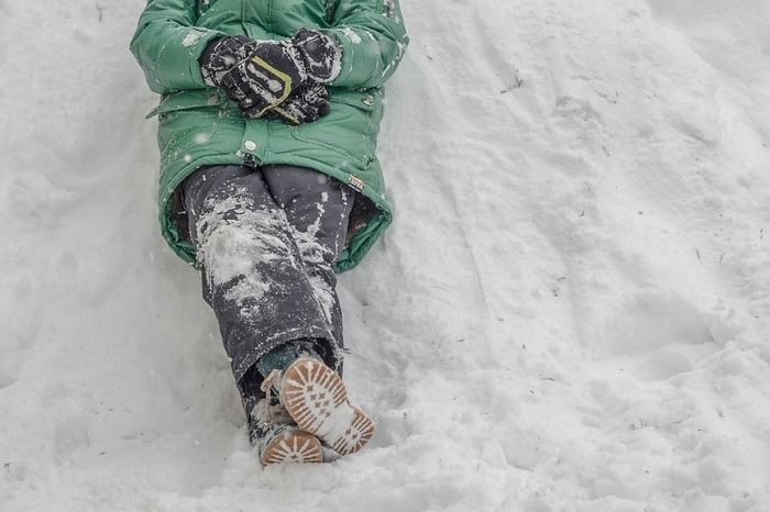 雪がついたスノーウェアを着て雪の上に寝転ぶ人