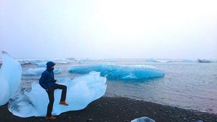 氷河の上に腰掛けるマウンテンパーカーを着た男性