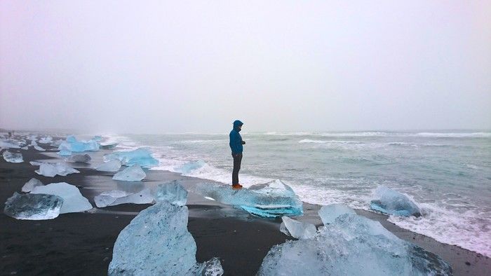 氷河の流れついた砂浜に立ち、海を見つめるマウンテンパーカーを着た男性