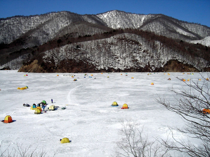 雪山のふもとでワカサギ釣りのを楽しむ人々