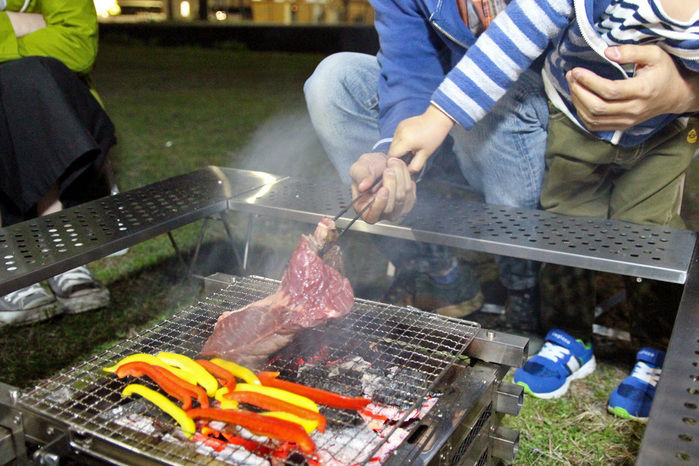 バーベキューで大きな肉を焼く親子