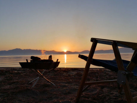 夕日の沈む池の水平線と焚き火とチェア