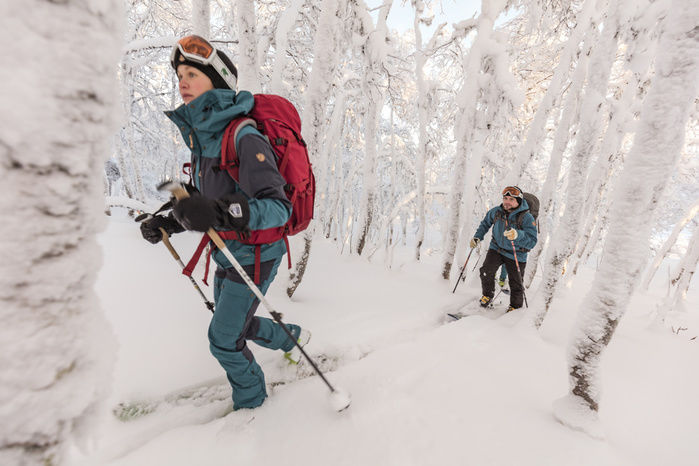 フェールラーベンのウェアを着て雪に覆われた山道を歩く人々