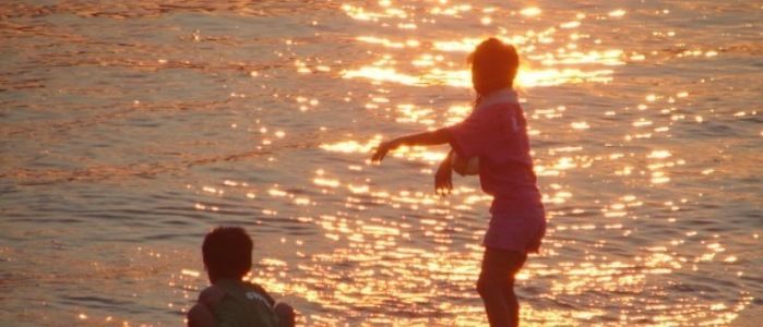 夕日を反射する海辺で遊ぶ少年の後ろ姿