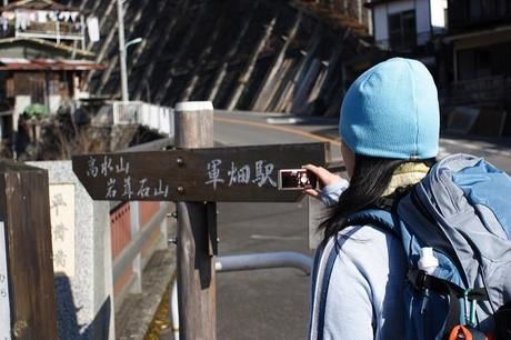 高水山岩葺石山と軍畑駅方面に分かれる案内表の写真を撮る女性