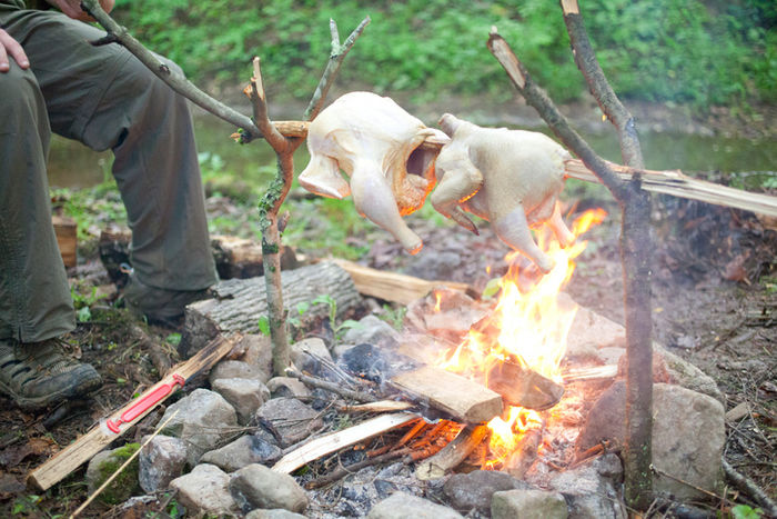 たき火で鶏肉の丸焼きを作る様子