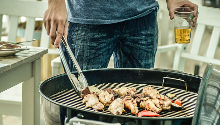 ビールを片手にバーベキューで肉を焼いている男性