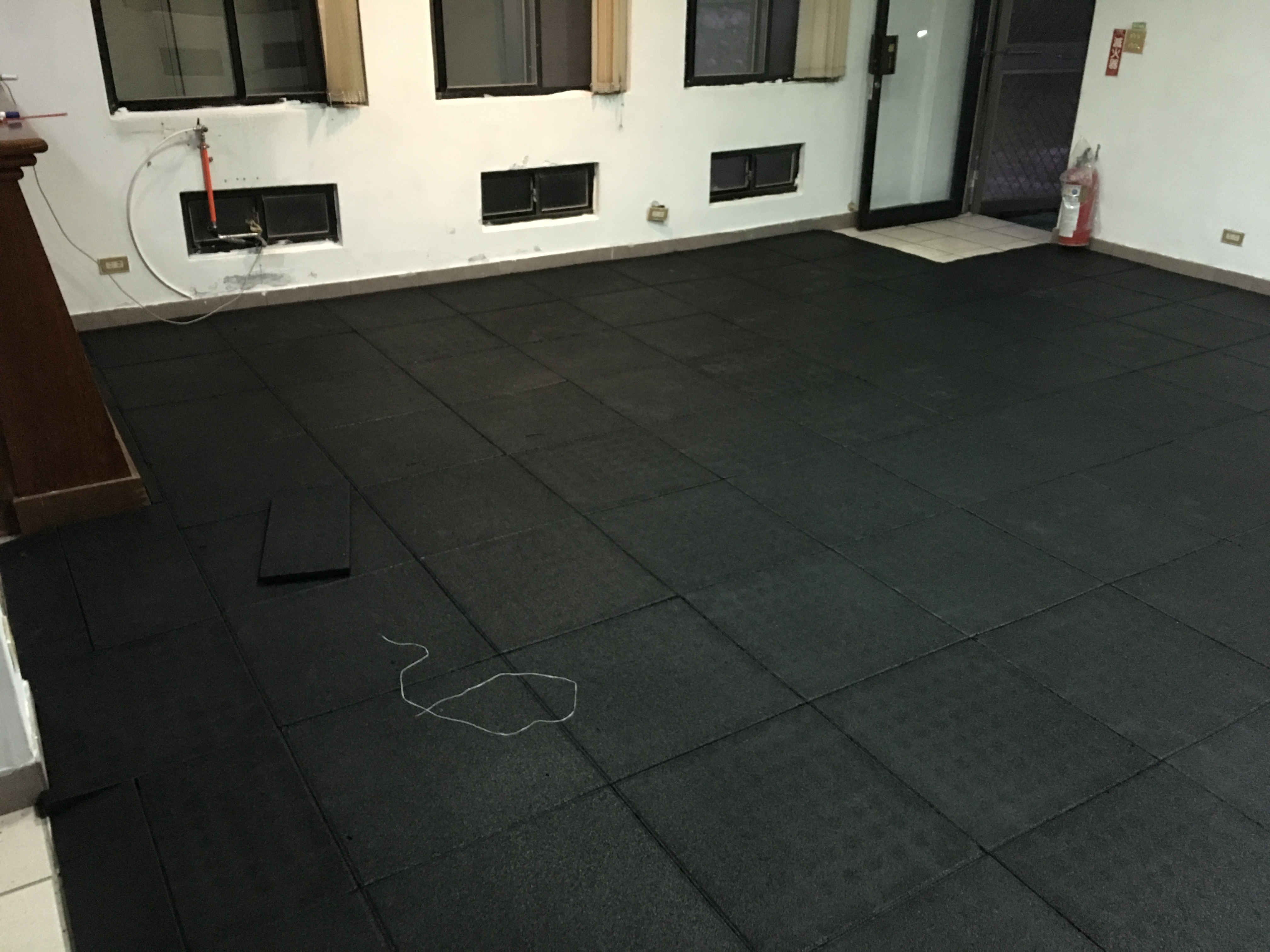 1) 照片顯示一個黑色橡膠地墊，鋪設在白色牆壁和木地板的房間裡