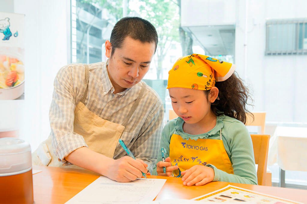 調理のレクチャーをメモをしながら真剣に聞/東京ガス キッズインザキッチン 親子クラス