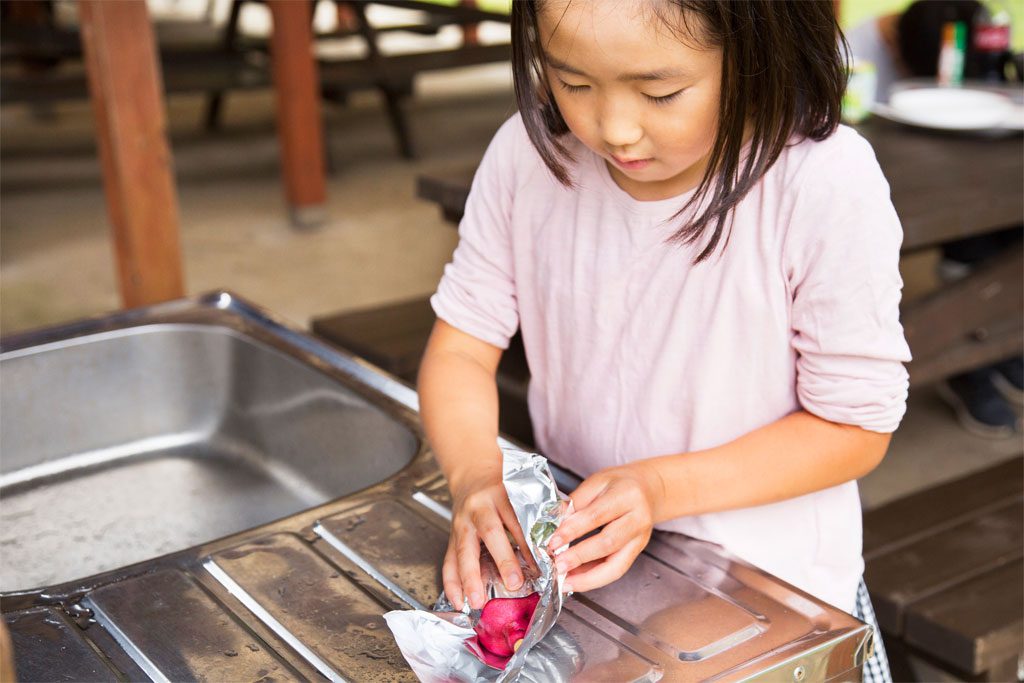 さつまいもをアルミホイルで包む女の子/7歳以上におすすめバーべキューお手伝い