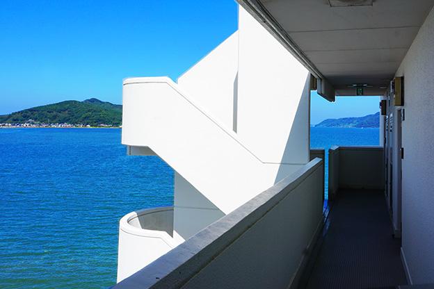 外から戻ってきて共用部廊下を歩くとこの眺望。視界の半分が海です。