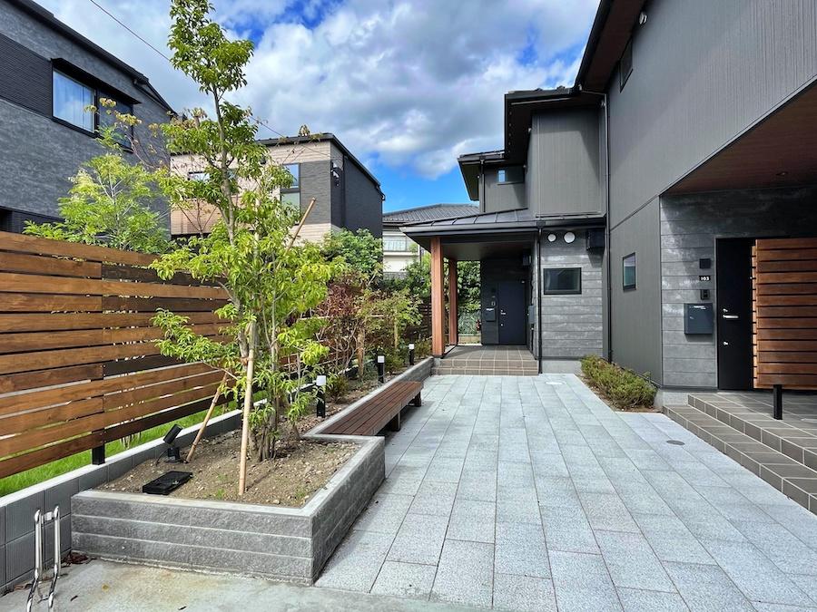 藤沢市鵠沼藤が谷三丁目の賃貸物件/ダークな外壁にウッドな壁の共有部｜ベンチの奥がバイク置き場で、かっこいいバイクが来てくれたらうれしい