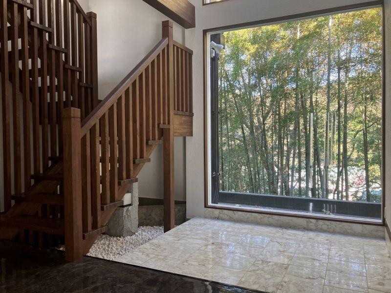 鎌倉市津の売買物件/ホール｜めいっぱい竹林が広がるFIX窓の手前は大理石貼り。木製の階段はがっしりしていながらも端正な印象。