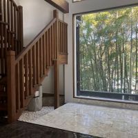 鎌倉市津の売買物件/ホール｜めいっぱい竹林が広がるFIX窓の手前は大理石貼り。木製の階段はがっしりしていながらも端正な印象。