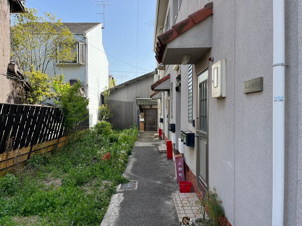 京都市北区紫野上柳町3の賃貸物件/手前の共同住宅に半分隠れるように建つ（草が生えてる空き地は他人地です）