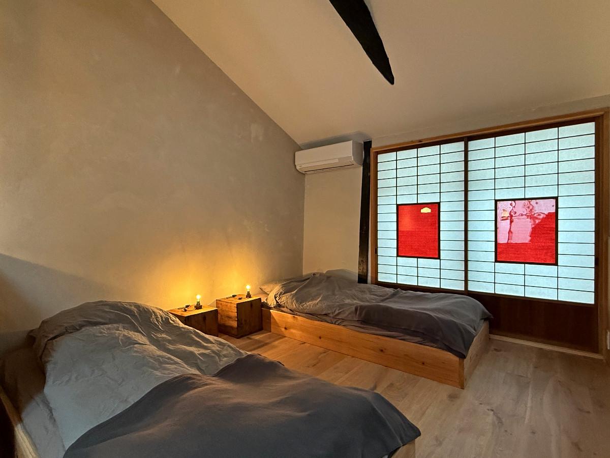 〒600-8141 京都府京都市下京区新日吉町１２４&minus;１０の賃貸物件/2階ベッドコーナー。町屋ですので、低めベッドでお布団風に。サイドテーブルにオリジナル照明がきらりと光ります。建具の赤もポップで日本人にはない感覚