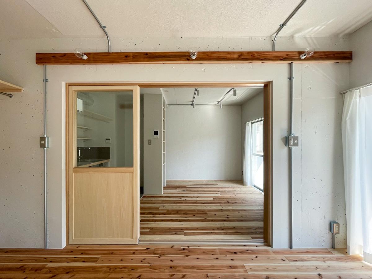 新宿区赤城下町の賃貸物件/西側の洋室からリビングを眺める。ガス管に収められた配線や、ステンレスのスイッチプレートが空間を引き締めている