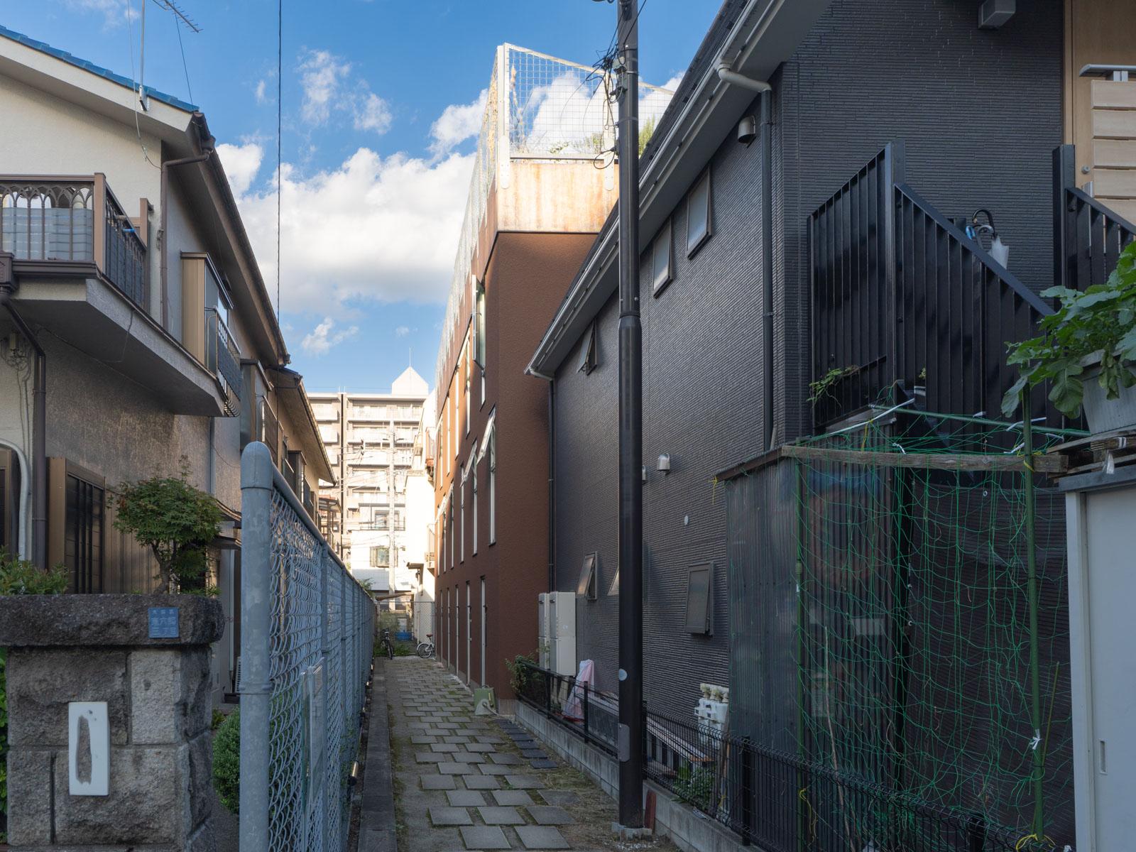 大田区東六郷の賃貸物件/建物外観。路地の先にあるブラウンの建物